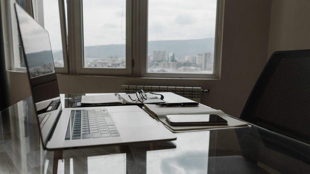 Glass office desk with open laptop notebook glasses and city view